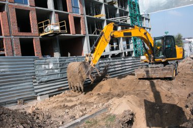 Çok katlı yeni bir binanın inşaatı. Temeli atarken kova kazıcı çalışması.