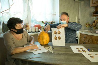 Jack O 'Lantern' i evde nasıl yaparım? Orta yaşlı bir adam ve kadın mutfakta Jack O 'Lantern' i beceriyorlar. İnsanların yüzlerinde maskeler var. Çift balkabağını nasıl düzgün keseceklerini tartışıyor..