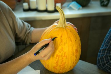 Jack O 'Lantern' i evde yapmak. Kalemle bir kadın eli, balkabağındaki kesik çizgilerini işaretler..