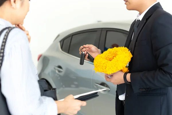 Salesman handing car keys to woman in showroom with greeting flower