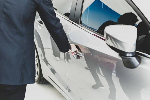 Family looking for new car with salemans hand on handle opening a car door in matte