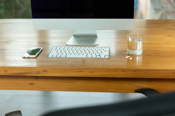 Conceptual work stress glass of water and pills on wooden desk with PC and cell phone