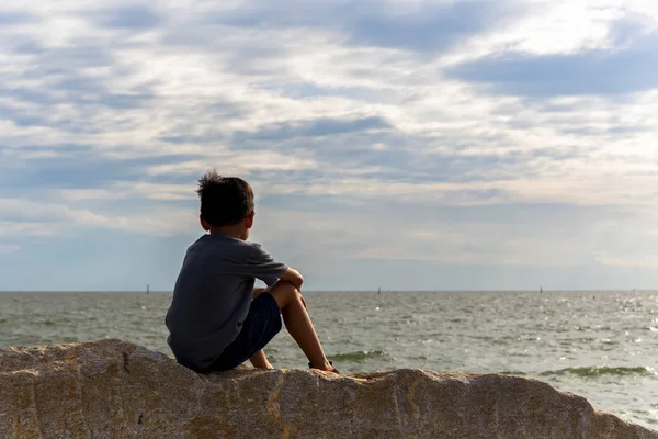 Chłopiec siedzi na skałach z widokiem na morze. — Zdjęcie stockowe