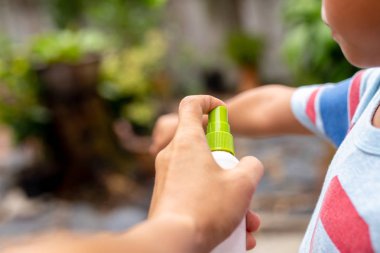 Father spraying insect repellents on his son arm in the garden. clipart