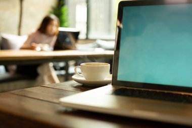 Seçilen odak fincan kahve ve arka planda çalışan bulanık kadın ile masa üstünde laptop.
