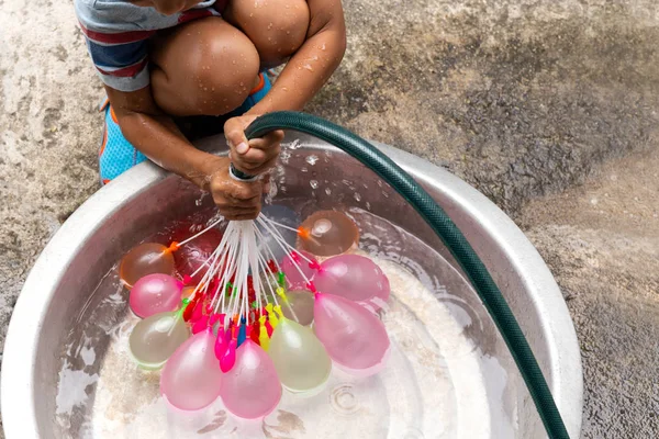 양동이에 화려한 물 풍선을 채우는 물 호스와 어린 소년. — 스톡 사진