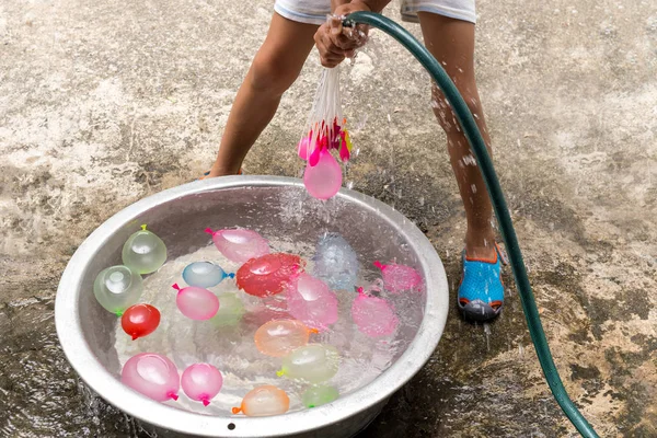 Niño pequeño con manguera de agua llenando globos de agua de colores en cubo . —  Fotos de Stock