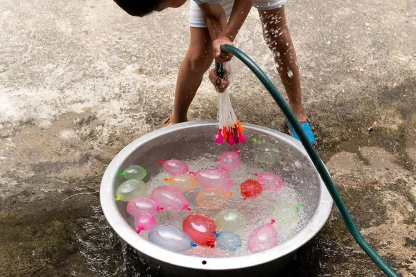 Маленький хлопчик з водяним шлангом, що заповнює барвисті водяні кульки у відрі . — стокове фото
