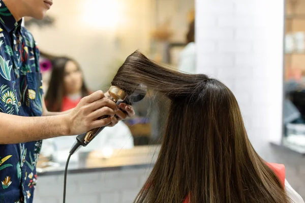 Peluquería estilista haciendo peinado usando secador de pelo soplado en el cabello del cliente en el salón de belleza . — Foto de Stock