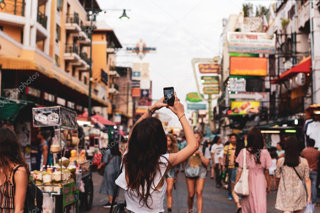 Woman tourist taking pictures with her cell phone on street in blurred background.