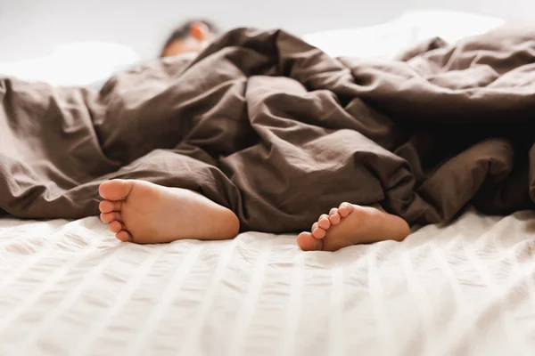 Giovane ragazzo piedi nudi a letto sotto coperta . — Foto Stock