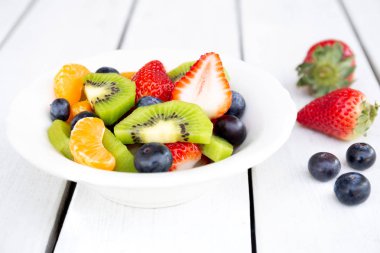 Beyaz ahşap masa üzerinde beyaz bir tabak içinde taze meyve salatası.