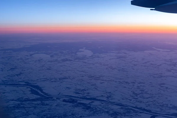 Aerial view from airplane window above land with snow and beautiful sunset. — Stock Photo, Image