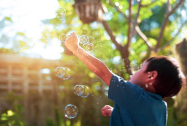 Bulanık kavramı genç çocuk güneş ışığı ile Bahçe kabarcık oyuncak ile oyun.