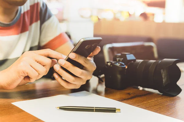 Mans kezében használ szúró telefon Dslr fényképezőgép és a toll több, mint a fából készült asztal papírmunka. — Stock Fotó