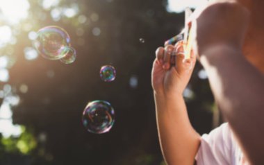 Blurred concept young child blowing bubble through bubble ring in sunlight. clipart