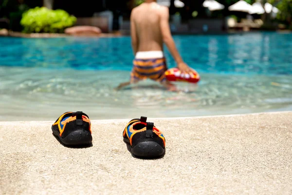 Zapatillas de baño al lado de la piscina con littel niño jugando con la pelota en fondo borroso . — Foto de Stock