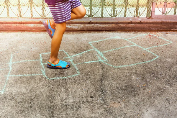 Niño jugando hopscotch juego en el suelo de hormigón al aire libre en verano . — Foto de Stock