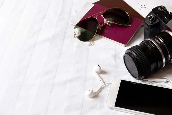 Κάτοψη του ταξιδιώτη αξεσουάρ στο κρεβάτι με ψηφιακή φωτογραφική μηχανή, κινητό, γυαλιά ηλίου και διαβατήριο. — Φωτογραφία Αρχείου