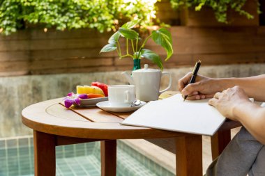 Tatile ahşap masa kahve fincanı ve taze meyve ile not defterinde yazılı işadamı el