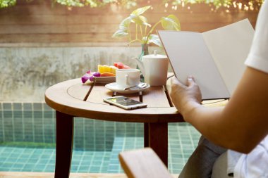 Ahşap masa fincan kahve ve taze meyve ile bir kitap okurken erkek