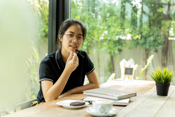 Asiam woman student eating cake with book and laptop in coffee shop