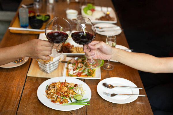 Friends celebration lunch with hands toasting glass red wine with food