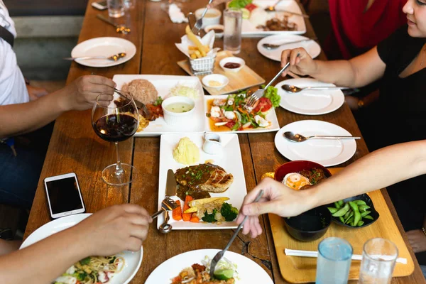 Group of friends hands with fork having fun eating variety food on the table