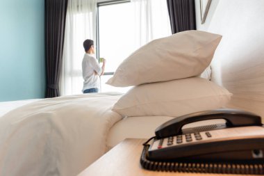 Pencerede fincan kahve ayakta tutan adamla otel odasında beyaz yastıklar