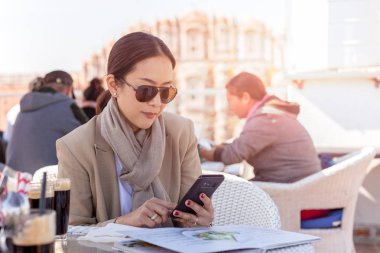 İş kadını rahat kafede otururken elinde cep telefonu bakarak güneş gözlüğü takıyor