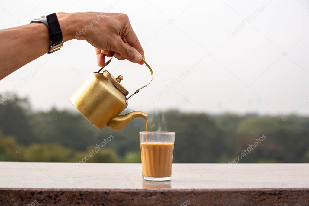 Hand pouring masala tea from a teapot into a glass