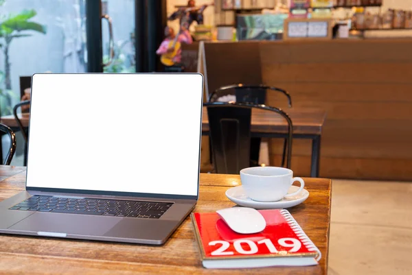 Blank screen laptop with mouse and coffee cup and notebook with Year 2019 calculator on table in cafe