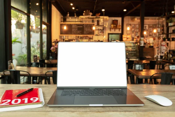 Laptop with mouse with blank screen and notebook with Year 2019 calculator on wooden desk in cafe