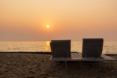 Okyanusu güzel gün batımını karşı sahilde iki boş şezlong.