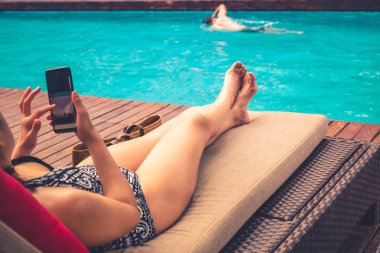 Güzel Bayan cep telefonuyla havuzda adamla sandalyenin üstüne yalan.