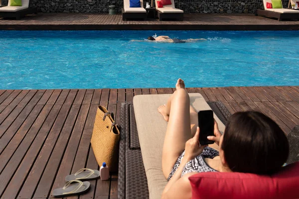 Hombre ejercicio de natación en la piscina con la mujer borrosa utilizando el teléfono celular en primer plano . — Foto de Stock