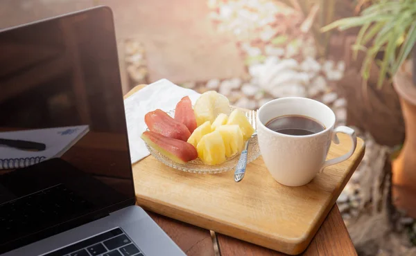 Kaffemugg med färsk frukt och laptop på träbord i trädgården. — Stockfoto