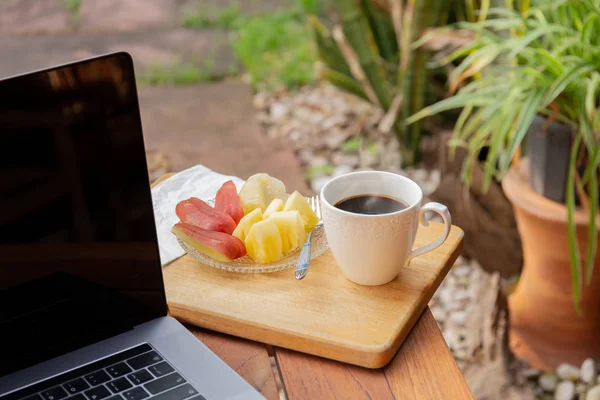 Kaffemugg med färsk frukt och laptop på träbord i trädgården. — Stockfoto