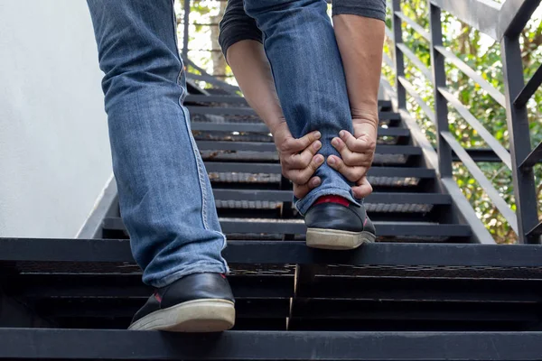 Mão de homem segurando o tornozelo doloroso enquanto subia as escadas . — Fotografia de Stock