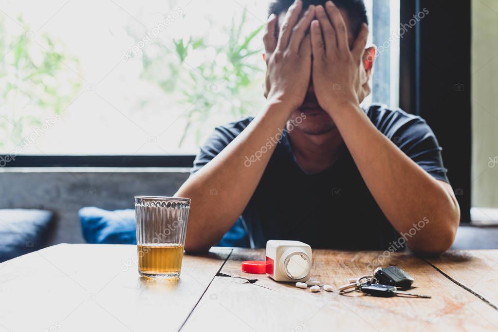 Depression man hand on his face with glass of alcohol and pills 