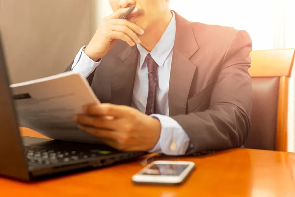 Empresario que lee el formulario del papeleo con el ordenador portátil en escritorio de madera . — Foto de Stock