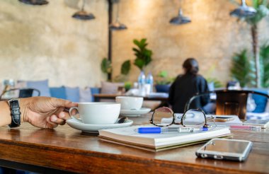 Okuma gözlüğü, ile kahve fincanı tablo cep telefonu tutan adam el.