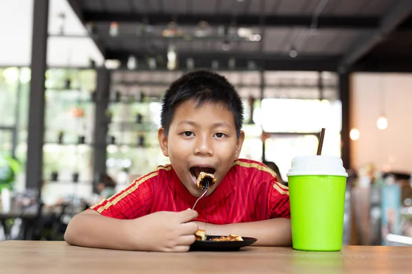 Feliz cara asiático chico disfrutar comer chocolate waffle en restaurante . —  Fotos de Stock