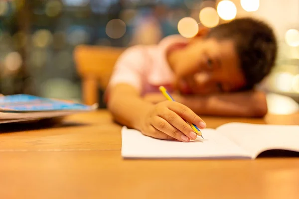 Asiático escuela chico celebración lápiz con cabeza en mesa mientras haciendo tarea . —  Fotos de Stock