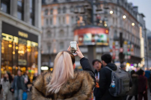 Mulher turista tirar fotos da cidade com seu telefone celular na rua em fundo embaçado . — Fotografia de Stock