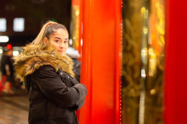 Kırmızı ışık ile pencerenin yanında duran kürk ceket ile Karışık ırk genç.