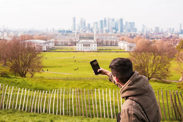 Młody człowiek turysta robi zdjęcia w parku z bulding miasta w tle. — Zdjęcie stockowe