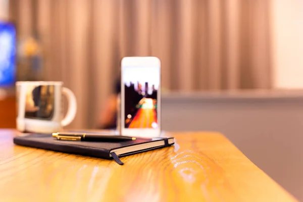 Cuaderno y bolígrafo con teléfono celular sobre mesa de madera en habitación de hotel . — Foto de Stock