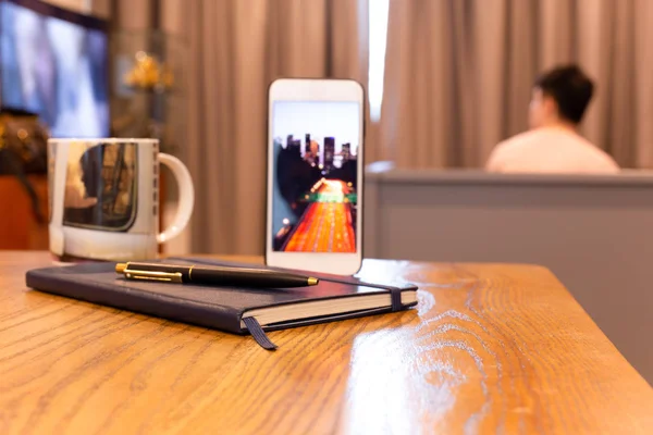 Notebook and pen with cell phone on wooden table in hotel room.
