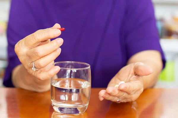Senior woman hands holding tablet with glass of water on table. — Stock Photo, Image